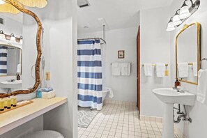 A bathroom with a vanity, a large mirror, a shower with a blue and white striped curtain, and a sink with a gold frame.
