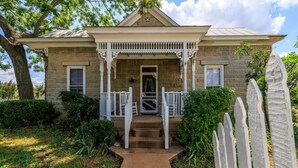 A two-story stone house with a porch, a front door, and a small staircase leading to the entrance. - Danz Haus | Historic Home | Baron's Creek (Fredericksburg)