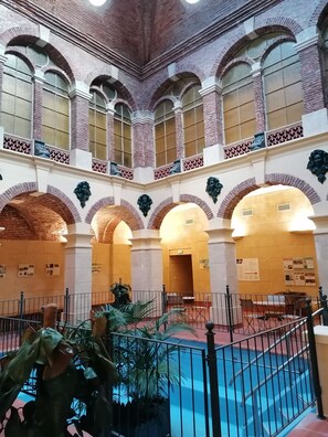 A courtyard with a pool, surrounded by brick arches and columns, with seating areas and informational posters on the walls.
