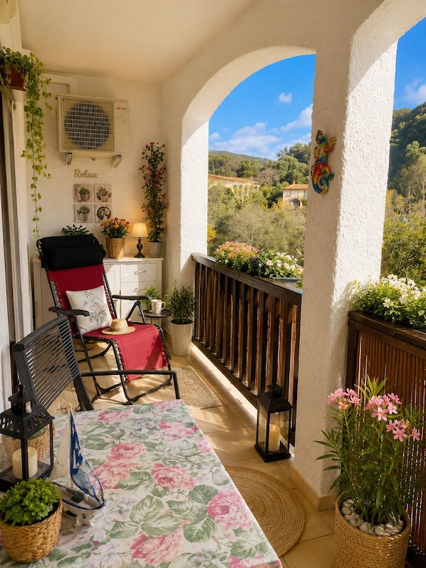 A balcony with a table, chairs, potted plants, and a view of the countryside.