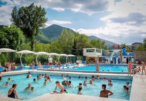 A swimming pool with multiple lanes, surrounded by trees and a mountain in the background.