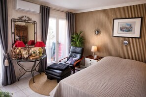 Ein Hotelzimmer mit einem Bett, einem Sessel, einem Nachttisch, einem Spiegel, einem Fenster mit VorhÀngen und einem Wandbild.