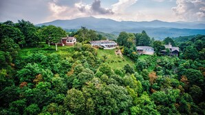 A large estate with multiple houses surrounded by dense forest and mountains in the background. - Celestial View (Blowing Rock)