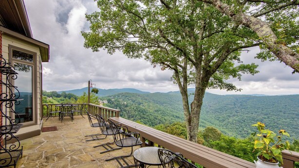 A patio with stone flooring, metal chairs, and a wooden bench overlooking a forested mountain range. - Celestial View (Blowing Rock)