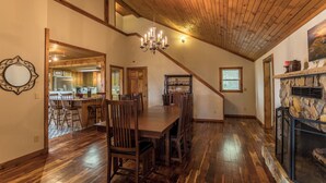 A dining area with a wooden table and chairs, a chandelier, and a stone fireplace. - Grandview Getaway (Deep Gap)