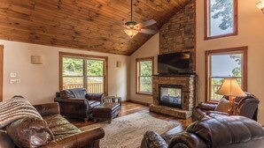 A spacious living room with a stone fireplace, leather furniture, large windows, and a wooden ceiling. - Grandview Getaway (Deep Gap)