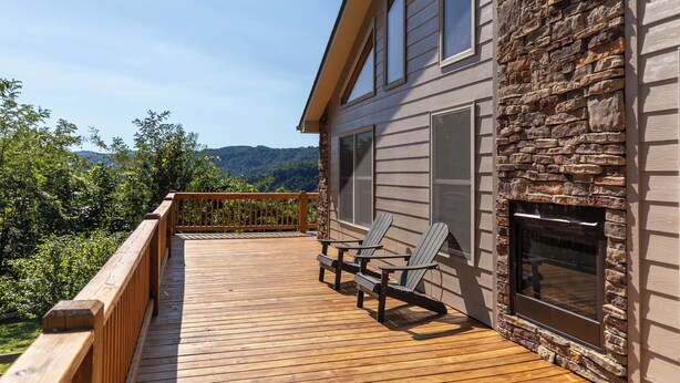 A wooden deck with Adirondack chairs, a stone exterior wall, and a large window. - Grandview Getaway (Deep Gap)