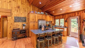 A wooden cabin kitchen with a central island, bar stools, a refrigerator, and a dining table. - Gait to Paradise (Boone)