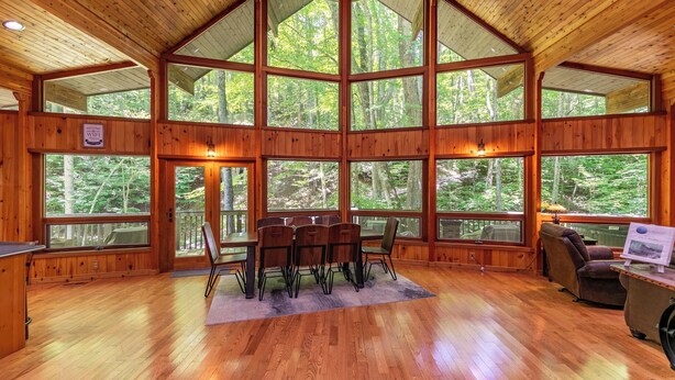 A spacious wooden cabin with large windows offering forest views, a dining area with a table and chairs, and a cozy seating area. - Gait to Paradise (Boone)