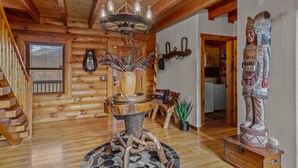 Ein Holzblockhaus-Innenraum mit einer Holztreppe, einer Kristallleuchtre, einem dekorativen Steinarrangement und einer Statue.
