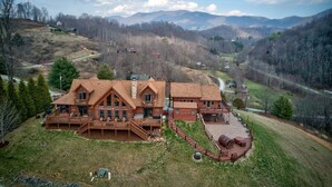 Eine große Holzhütte mit mehreren Terrassen und einer überdachten Veranda, umgeben von einer grünen Landschaft und Bergen.