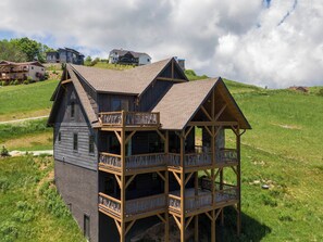 A wooden house with a balcony, surrounded by a grassy landscape and other houses in the background. - Constellation Prize at Monteagle (Banner Elk)