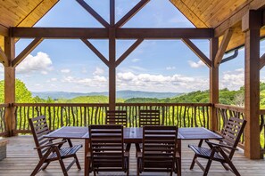 A covered outdoor seating area with a wooden table and chairs, overlooking a lush landscape. - Constellation Prize at Monteagle (Banner Elk)
