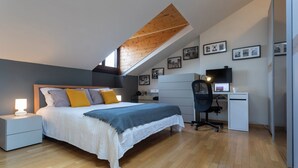 A bedroom with a bed, bedside table, desk, chair, and a sloped ceiling with wooden beams. - Belfiore Apartment by Wonderful Italy (Turin)