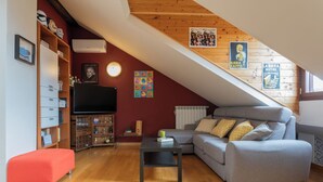 A cozy loft-style living room with a wooden ceiling, a grey sofa, a red ottoman, and a TV on a wooden shelf. - Belfiore Apartment by Wonderful Italy (Turin)