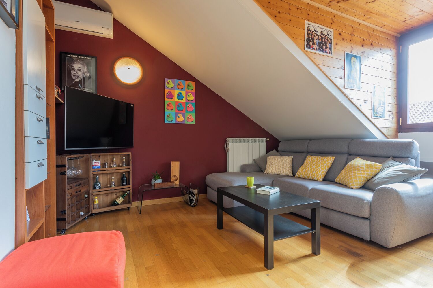 Una sala de estar acogedora con televisor, muebles de madera, un sofá y un sillón rojo.