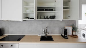 A kitchen with a black sink, white cabinets, and a grey backsplash. - BOHO Studio - Augarten City Apartment (Vienna)