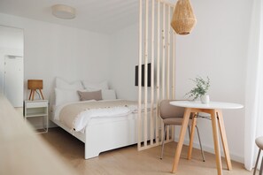 A bedroom with a bed, a bedside table, a chair, a small table with a plant, and a hanging light fixture. - BOHO Studio - Augarten City Apartment (Vienna)