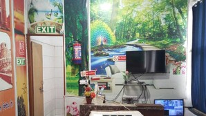 Een kamer met een grote muurschildering van een boslandschap, een televisie, een bureau met een computer en een airconditioning.