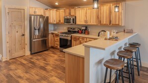 Una cucina moderna con mobili in legno, elettrodomestici in acciaio inossidabile e un'area bar con sgabelli.