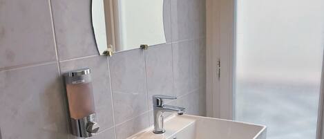 Un baño moderno con un lavamanos blanco rectangular, un grifo de cromo y un espejo fijado a la pared.