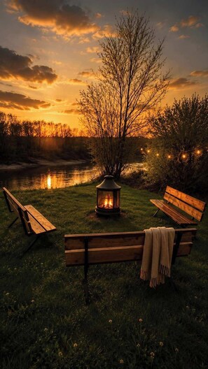 Un cadre extérieur paisible, avec un banc en bois, une lanterne et une rivière au coucher du soleil.