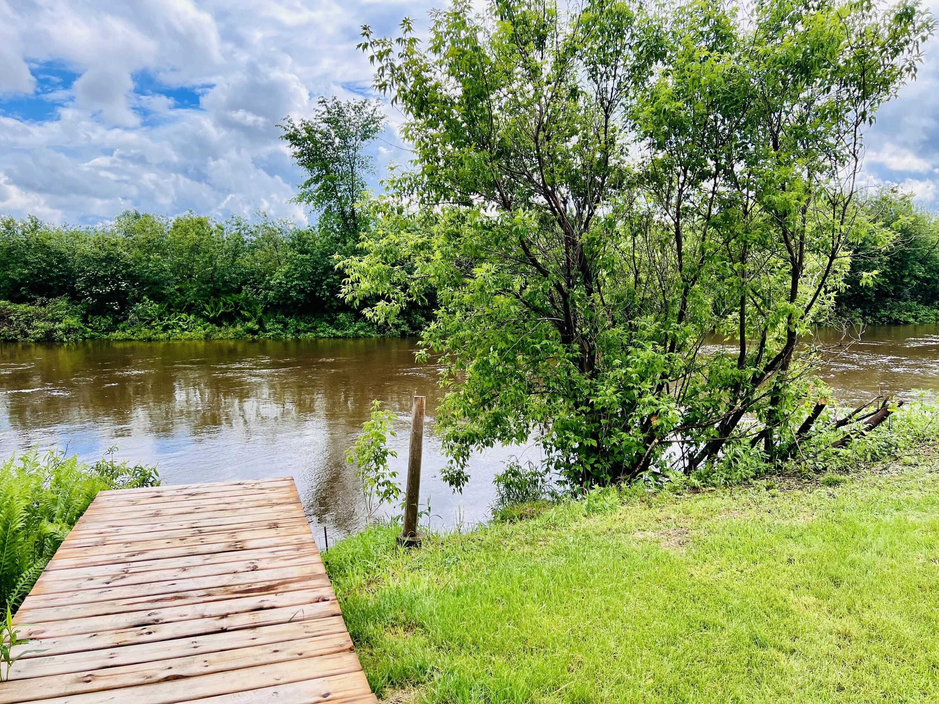 Une jetée en bois s’étendant dans une rivière, entourée d’une végétation luxuriante et d’arbres.