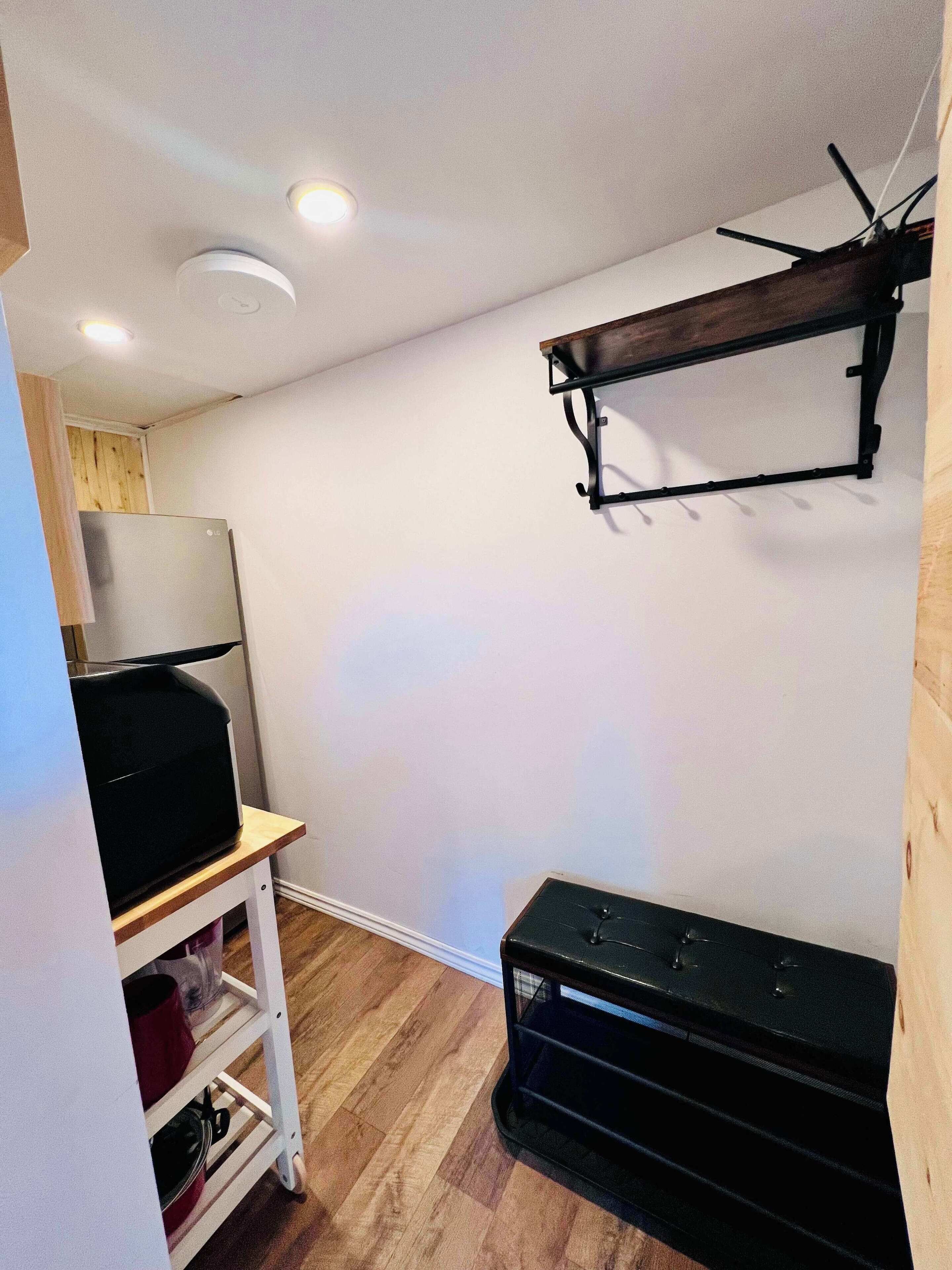 A compact kitchen with a refrigerator, a wooden shelf, and a black appliance on the floor.