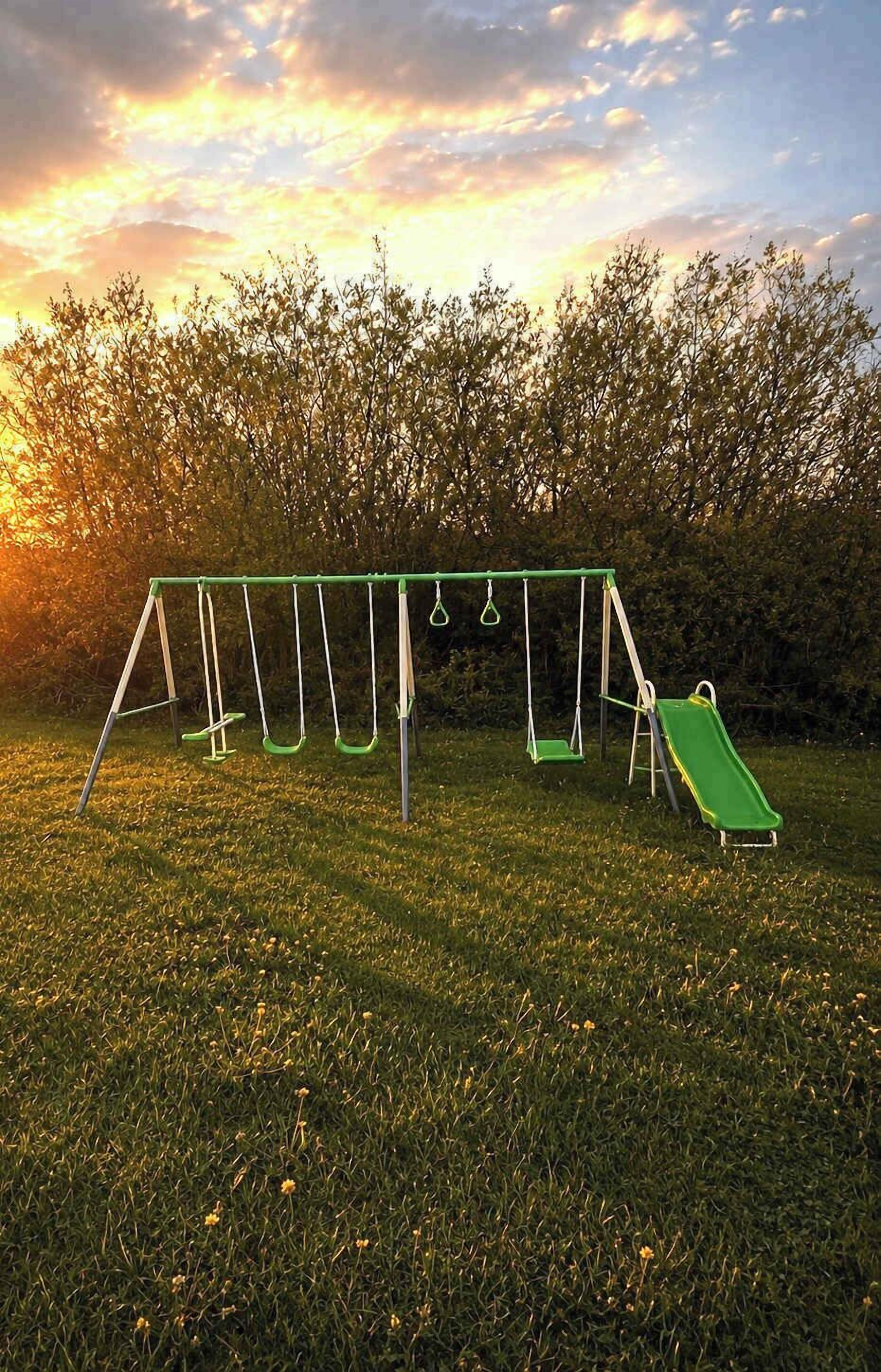 Eine Schaukel auf einer grünen Wiese, im Hintergrund ein Sonnenuntergang.