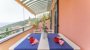 A balcony with a table set for two, covered by a striped awning, overlooking a scenic view of a hill and a church. - Emma House, Terrace and Sea View, Moneglia (Moneglia)