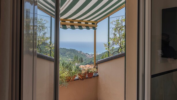 A balcony with a striped awning, potted plants, and a view of the sea and hills. - Emma House, Terrace and Sea View, Moneglia (Moneglia)