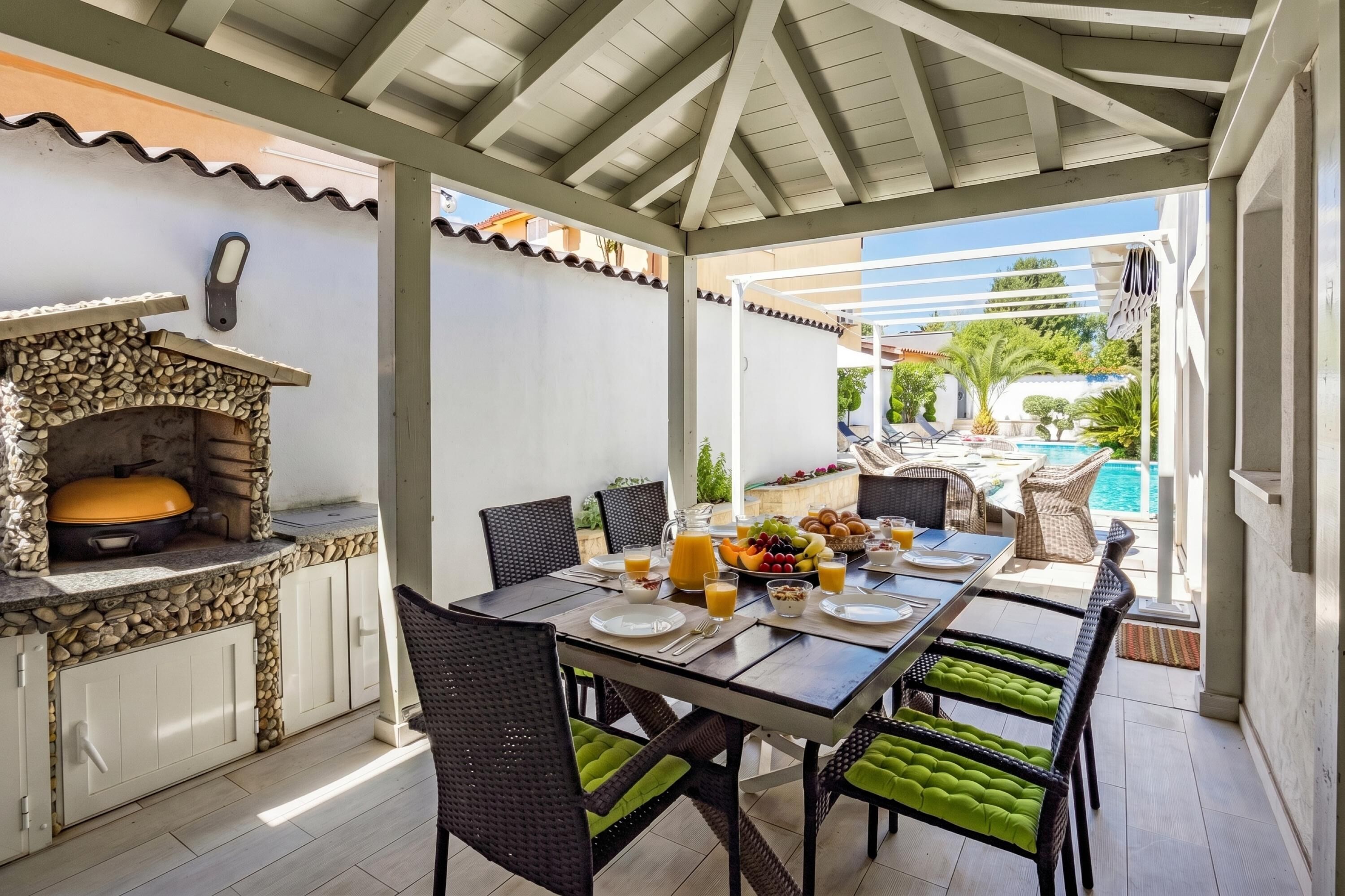 An outdoor dining area with a stone fireplace, wicker chairs, and a view of a pool.