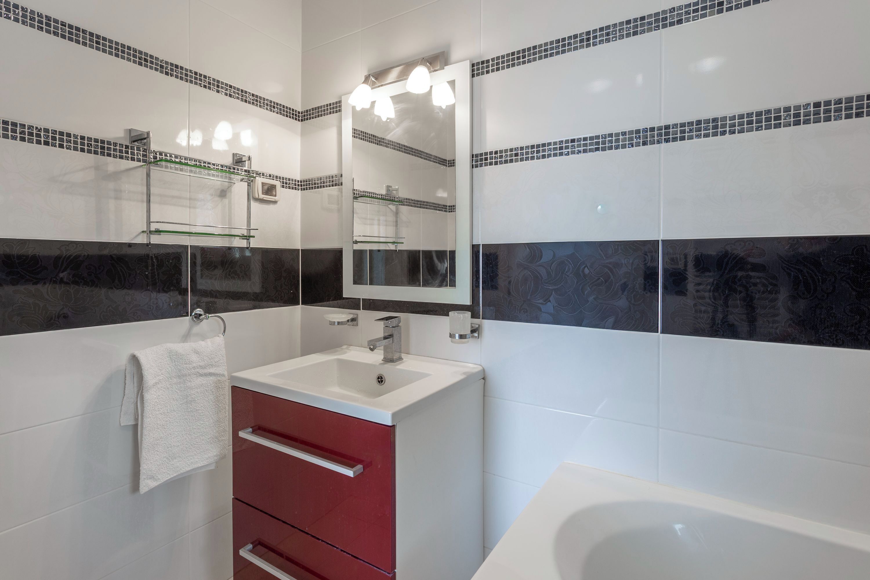 A modern bathroom with a white sink, red cabinet, and a large mirror above it.
