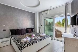 A modern bedroom with a zebra-patterned bedspread, a glass door leading to a balcony, and a mounted TV. - Villa Bianco Nero (Pula)