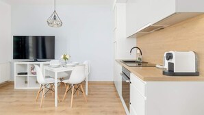 A modern kitchen with white cabinetry, a wooden countertop, a built-in oven, and a coffee machine.