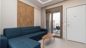 A modern living room with a blue sofa, a wooden coffee table, and a sliding glass door leading to an outdoor area. - SithoniaRS Seashell Maisonette (Νικήτη)