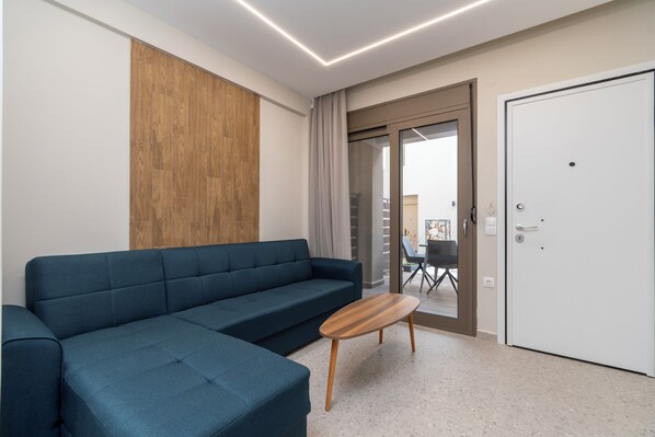 A modern living room with a blue sofa, a wooden coffee table, and a sliding glass door leading to an outdoor area.