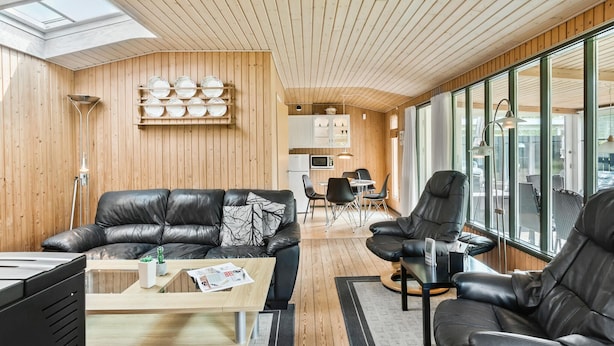Ein modernes Wohnzimmer mit Ledersofas, einem Holzesstisch und einer Küchenzeile mit Schränken und einer Mikrowelle.