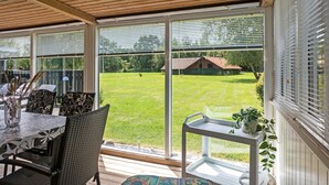 Eine überdachte Terrasse mit Tisch, Stühlen und Blick auf einen Rasen.