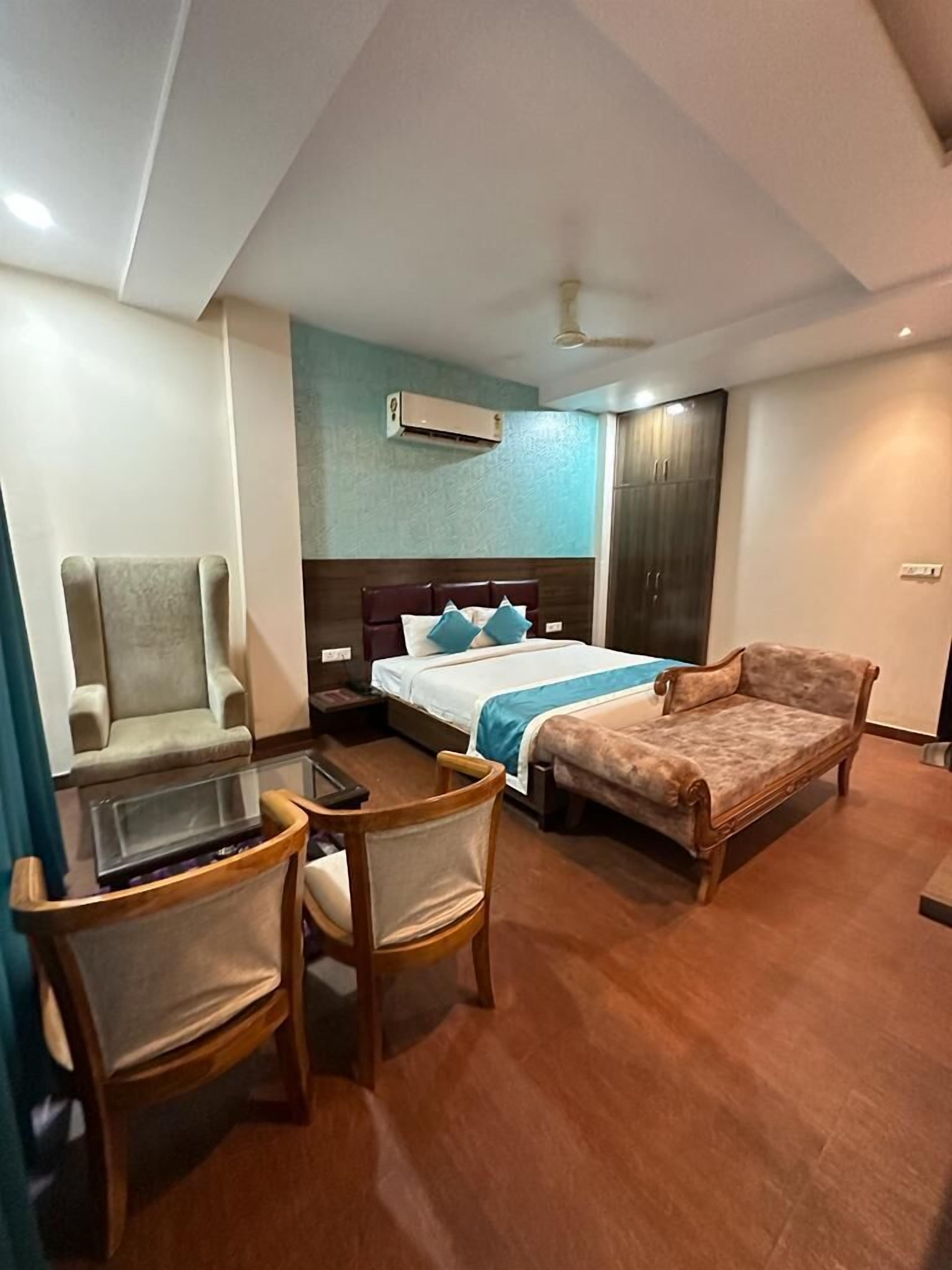 A hotel room with a bed, a sofa, a desk with chairs, and a ceiling fan.