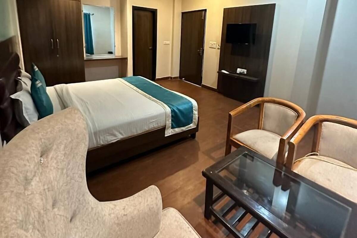Una habitación de hotel moderna con una cama, dos sillas, una mesita de vidrio, un televisor y un armario.