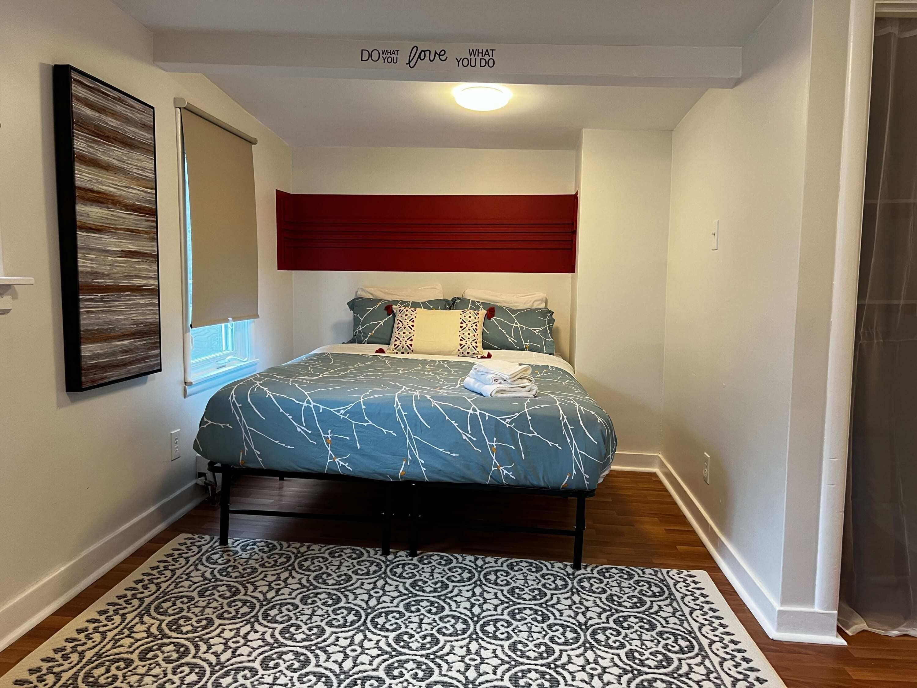 A bedroom with a bed, a patterned rug, a red headboard, and a motivational quote on the wall.