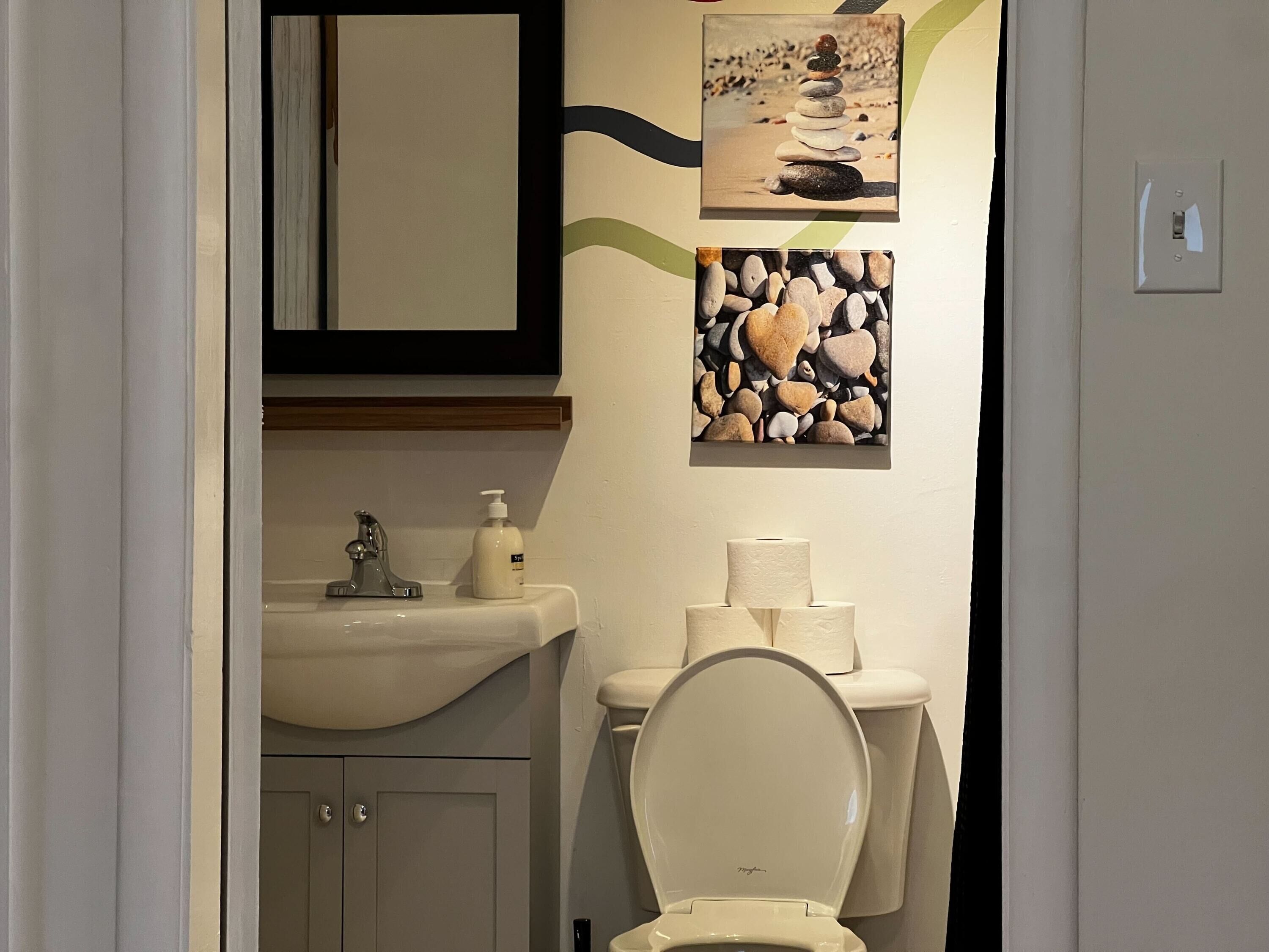 A bathroom with a toilet, sink, and two framed pictures on the wall.