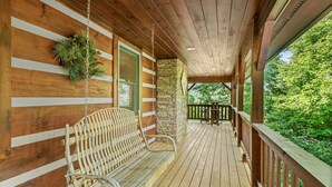 Un portico in legno con una panchina, una pianta pensile e un pilastro in pietra.