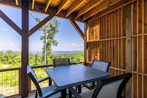 A wooden deck with a table and chairs, overlooking a mountainous landscape. - Mountain Kandy at Blue Ridge Mountain (Lenoir)