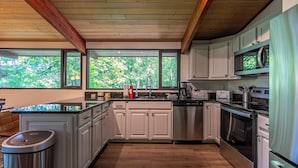 A modern kitchen with white cabinets, stainless steel appliances, and a large window overlooking greenery. - Chasing Birdies (Banner Elk)