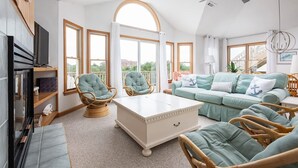 A spacious living room with a large window, a ceiling fan, and a sofa with anchor-themed pillows. - Private pool/spa, rooftop deck, 5min walk to beach (Corolla)