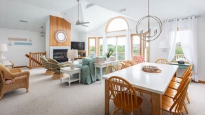 A spacious living room with a fireplace, a dining area with wooden chairs, and a large window offering a view of the outdoors. - Private pool/spa, rooftop deck, 5min walk to beach (Corolla)