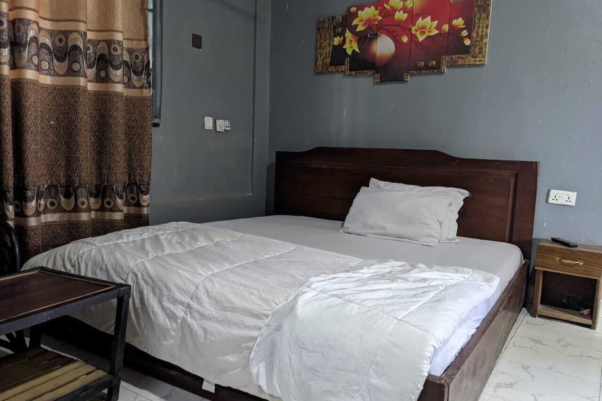 A single bed with a white duvet, a wooden headboard, a nightstand, and a wall with a floral artwork.