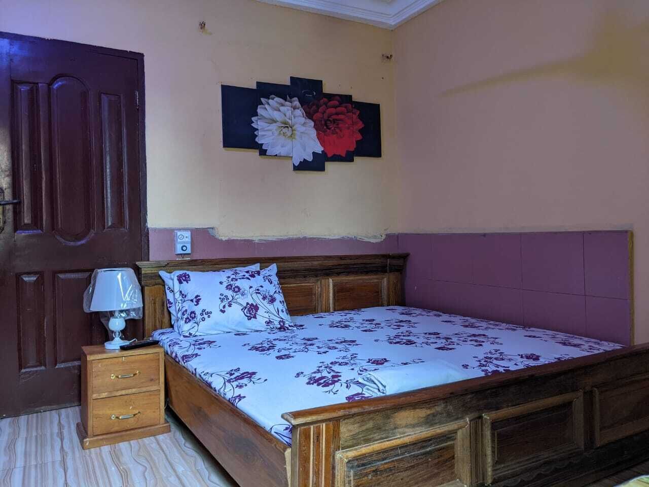 A bedroom with a wooden bed, a nightstand with a lamp, a door, and a wall-mounted artwork.
